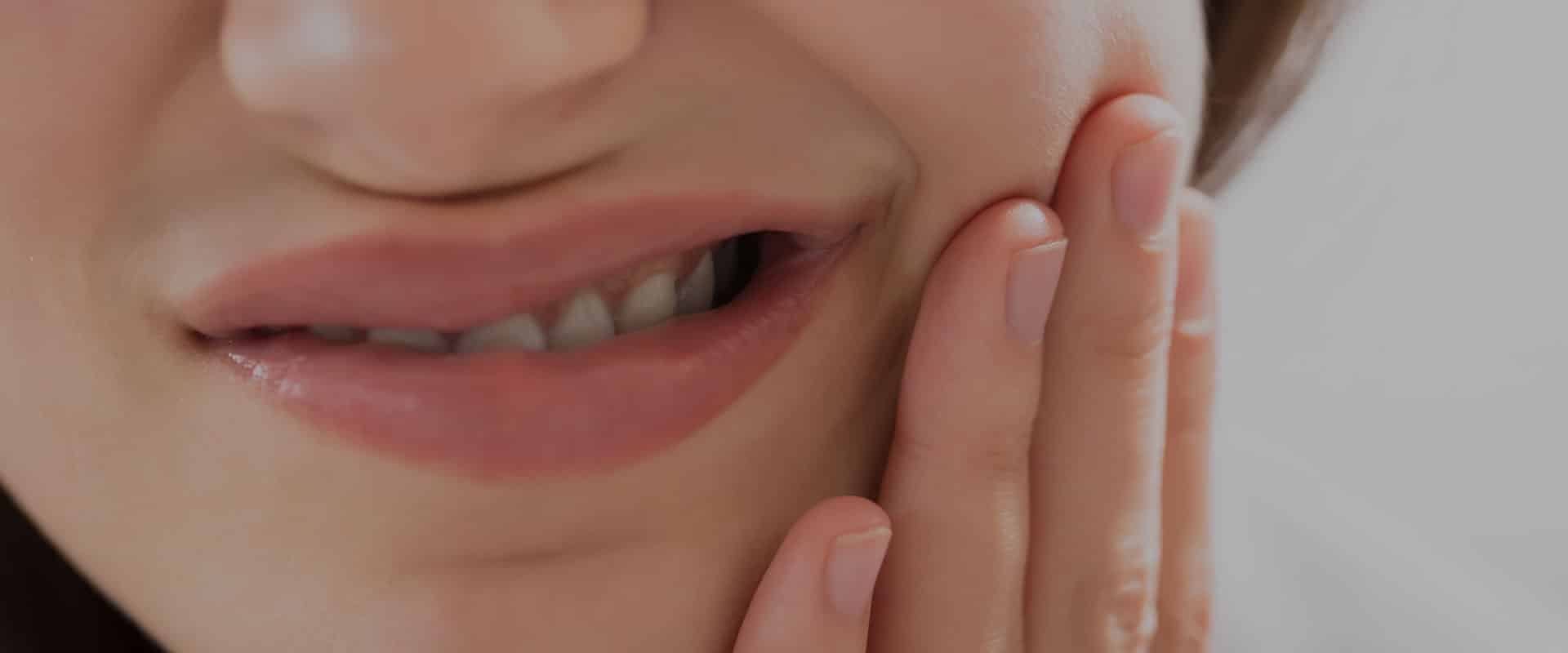 Person touching cheek due to tooth sensitivity caused by cold foods or drinks