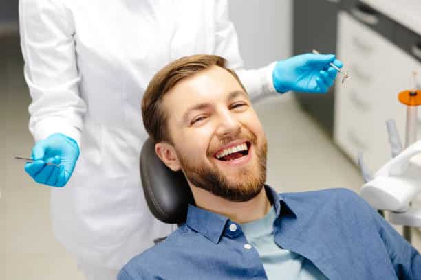 Smiling patient sitting in a dental chair during a consultation while a dentist prepares for an oral examination.