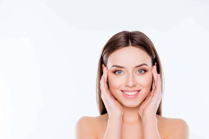 Smiling woman gently touching her face with both hands for a refreshed facial appearance